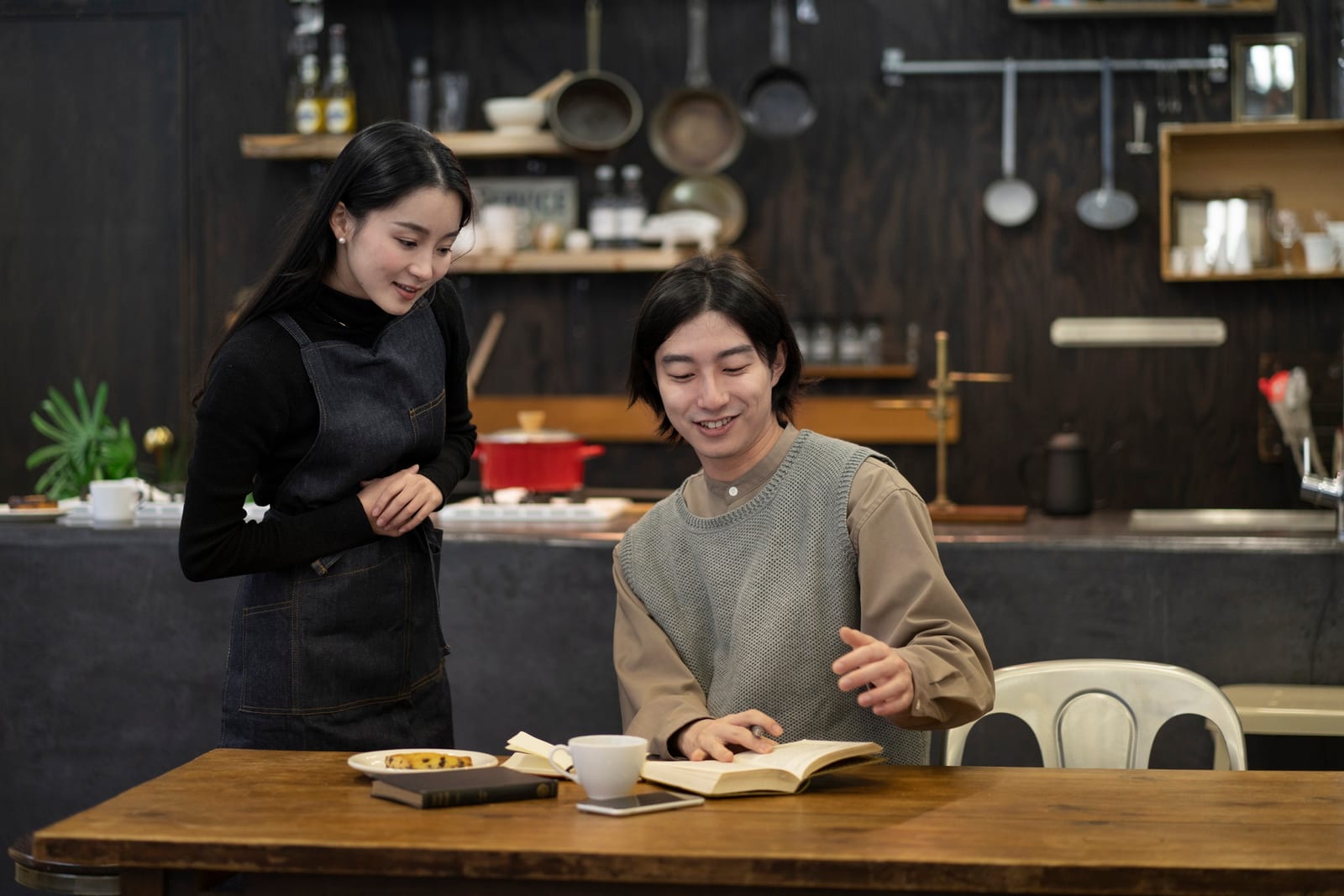 キッチンのテーブルで本を読む男性と、そばで見守るエプロン姿の女性