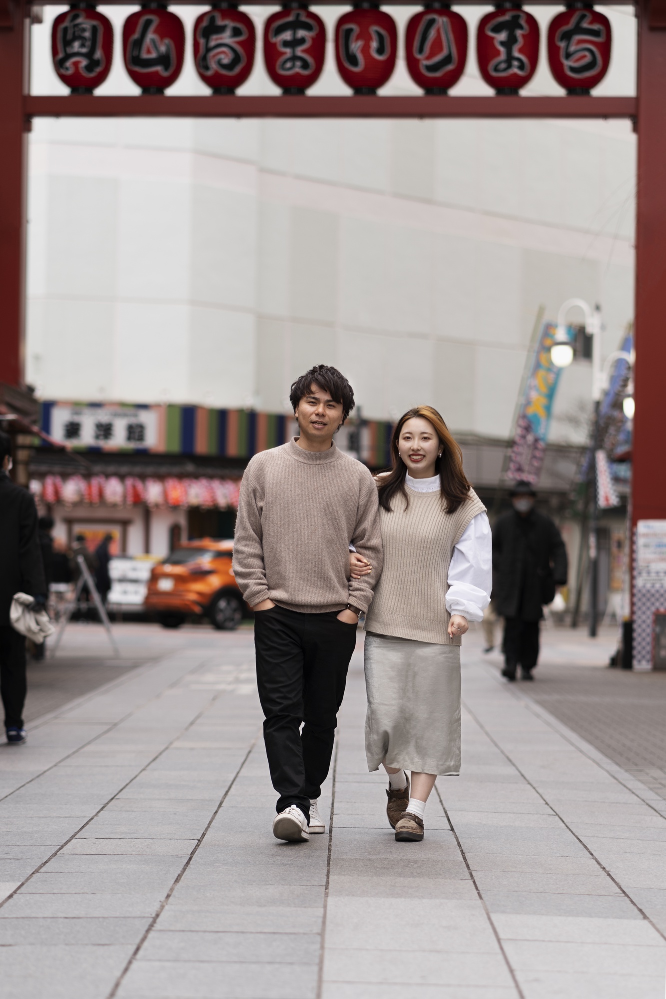 提灯の下がる商店街のアーチをくぐって歩く、若いカップルの後ろ姿
